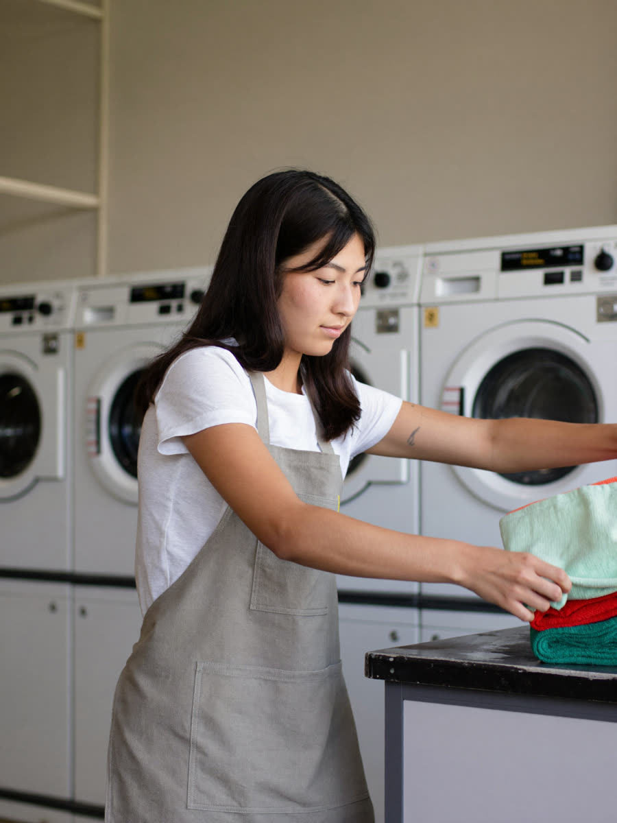 Filipino laundromat attendant folding laundry in front of washing machines